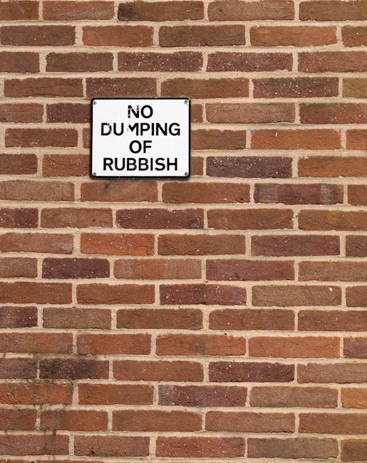 A person wearing a light-colored long-sleeve shirt is seen discarding crumpled brown paper into a small, round, wooden trash bin with a smooth finish. The person's hand is positioned above the open to